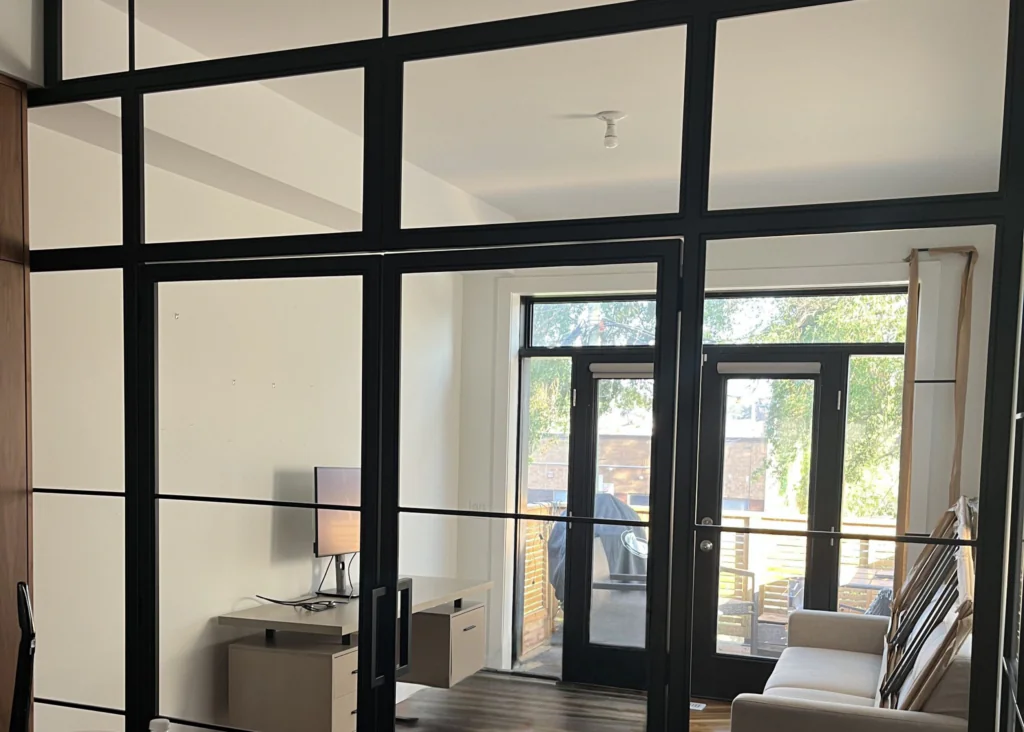 Black metal-framed glass room divider with rectangular panels separating interior spaces