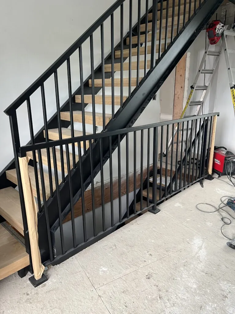 Industrial open riser staircase with double metal stringers and vertical picket railing, featuring a durable steel structure and modern industrial design.