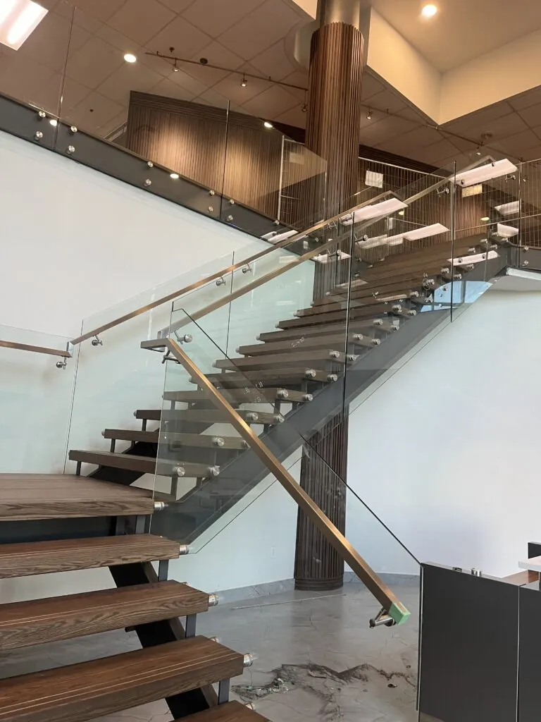 Commercial double stringer staircase with glass railing and offset handrail, featuring a modern steel structure and tempered glass panels.
