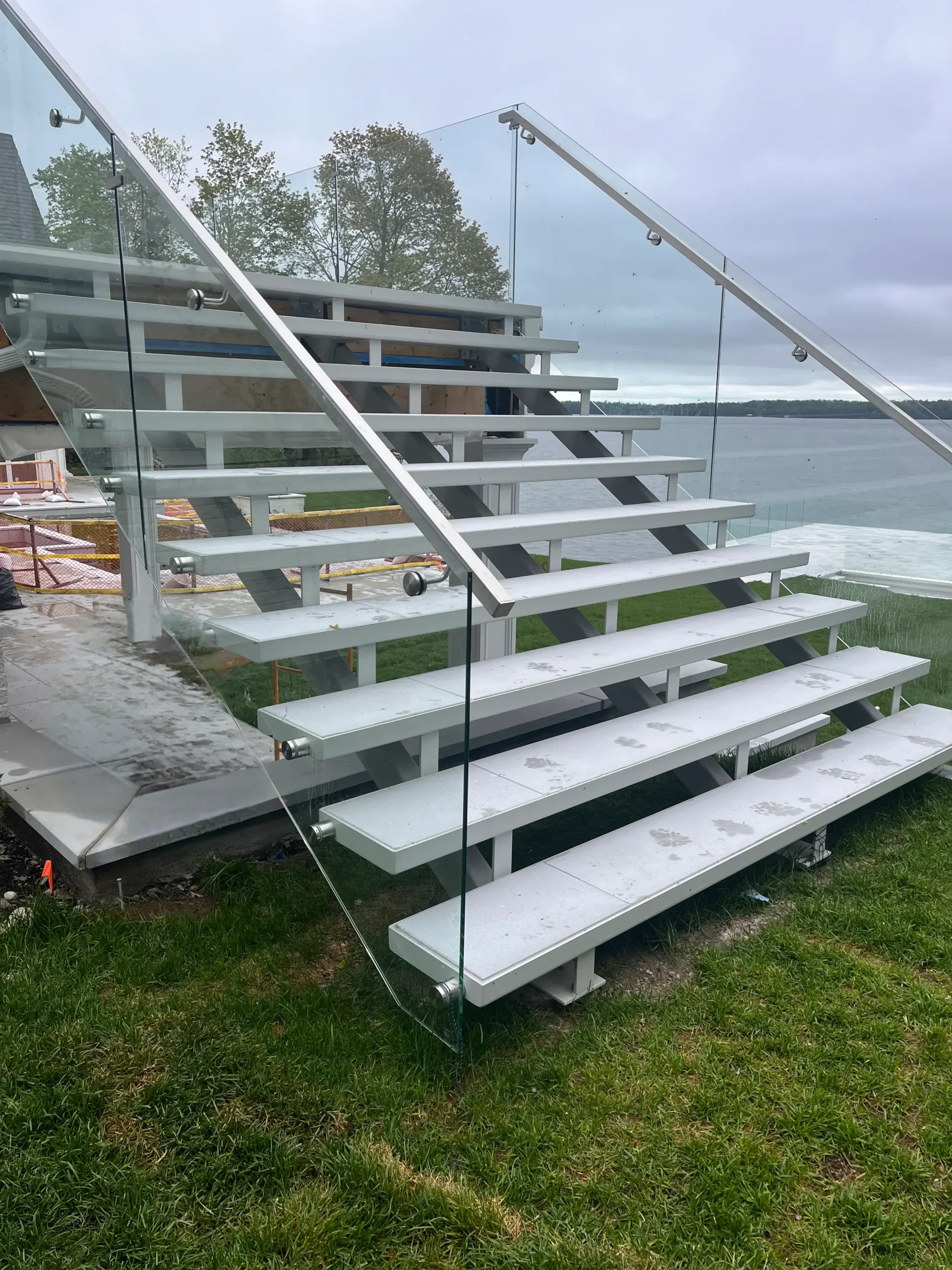 Outdoor metal staircase with open treads and glass railings.