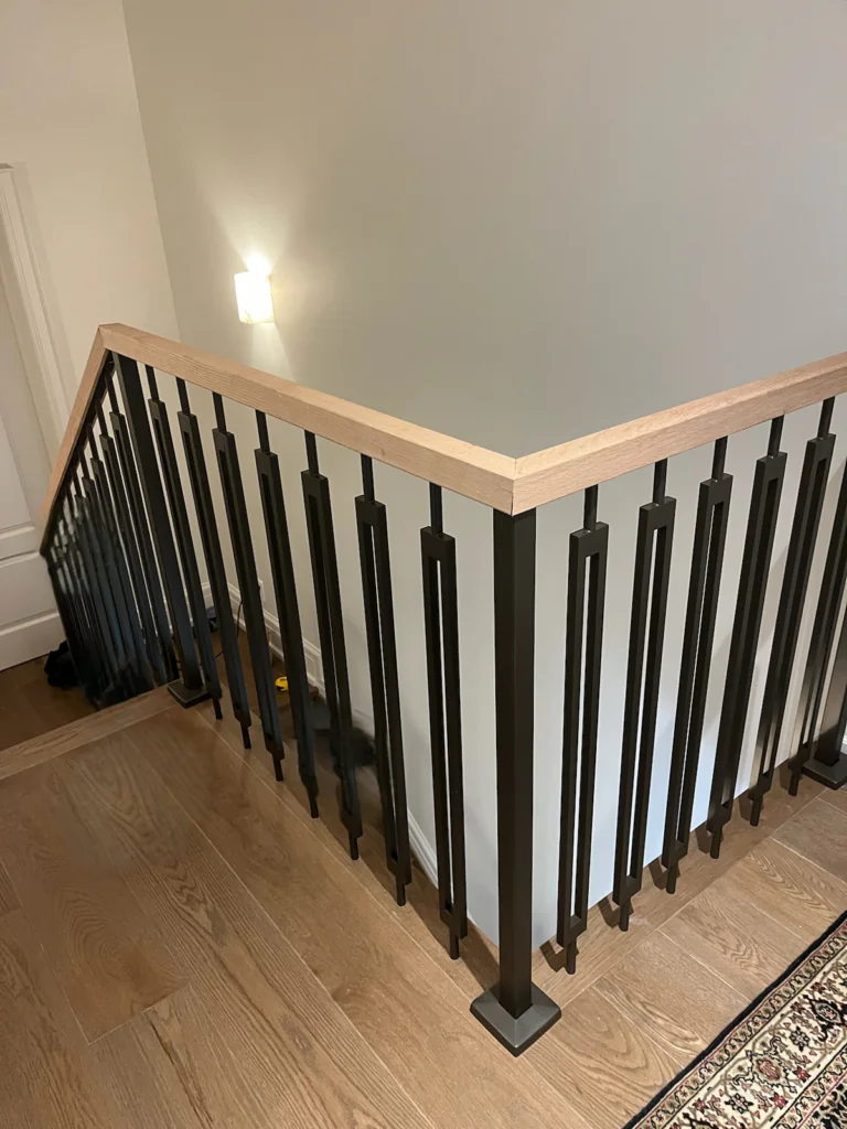Decorative black metal stair railing with vertical pickets and a natural wood handrail