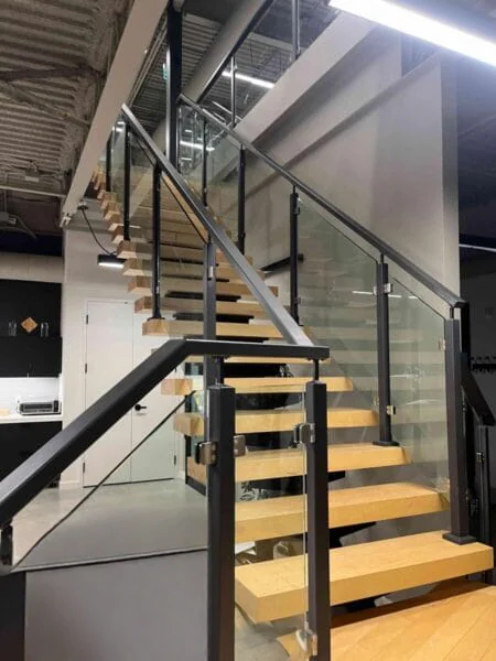 Open-riser staircase with wood treads, glass railing panels and black metal posts and handrails.