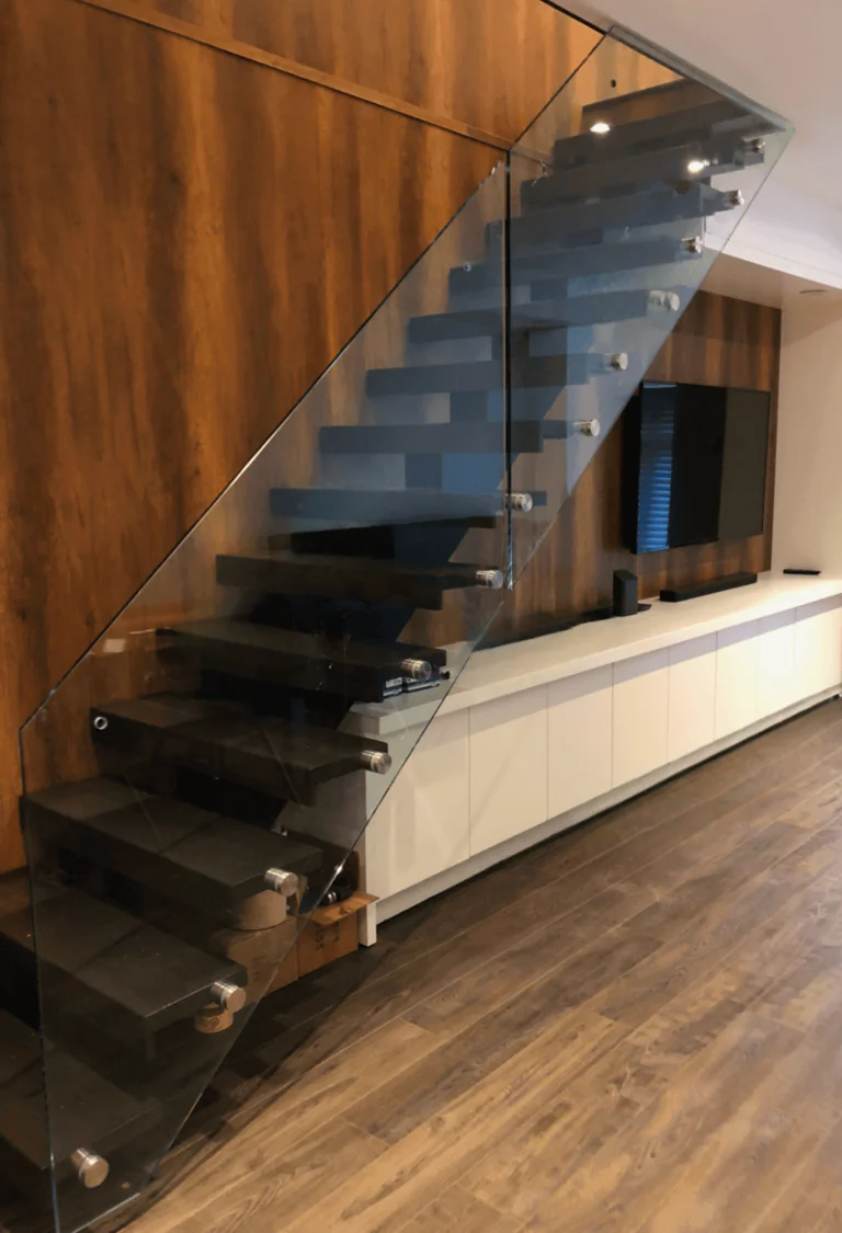 Mono beam staircase with dark wood treads and glass railing beside a wood panelled wall.